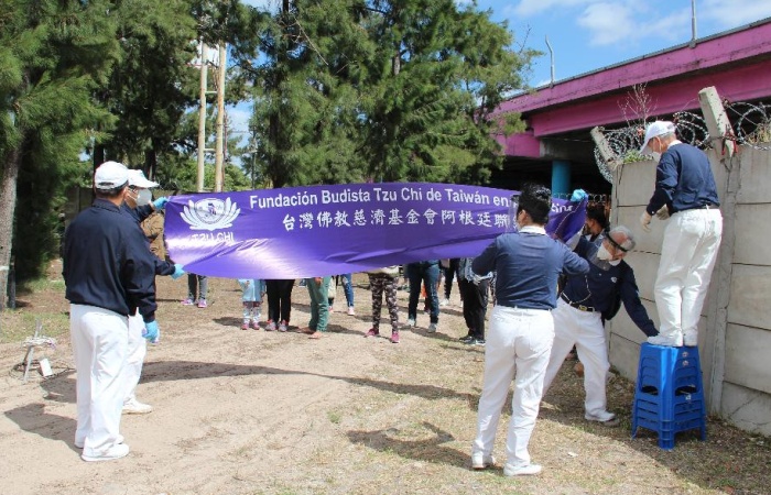 強風攪局,增加了掛布幔的時間,掛上去不一會兒又被吹落了,只好由兩位志工拉著布幔。(攝影者:鍾貴滿,地點:魯漢村退休老人中心預定地,日期:2020/12/20)
