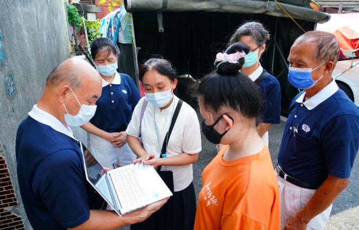 學子欣宜(化名)的家簡陋髒亂狹窄,志工們只好在對面空地來頒贈筆電並說明使用方法。(攝影者:詹大為,地點:彰化埔心鄉,日期:2021/08/21)